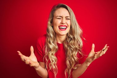 Genç güzel kadın kırmızı izole arka plan üzerinde duran temel t-shirt giyen deli ve silah ile başarı için deli kutluyor kaldırdı ve heyecanlı çığlık kapalı gözleri. Kazanan kavramı