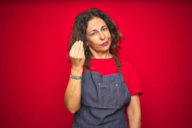 Kırmızı izole arka plan üzerinde apron üniforma giyen orta yaş kıdemli kadın el ve parmaklar ile Italyan jest yapıyor emin ifade