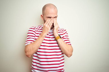 Sakalı genç kel adam, yorgunluk ve baş ağrısı, Uykulu ve yorgun ifade için beyaz izole arka plan sürtünme gözleri üzerinde rahat çizgili kırmızı t-shirt giyiyor. Vizyon sorunu