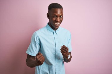 Afrika Amerikan adam izole pembe arka plan üzerinde ayakta mavi rahat gömlek giymiş çok mutlu ve heyecanlı silah kaldırdı, gülümseyen ve başarı için çığlık ile kazanan jest yapıyor. Kutlama konsepti.