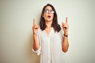 Beyaz izole arka plan üzerinde ayakta gömlek ve gözlük giyen genç güzel kadın hayran ve parmak ile işaret, el ile sunmak ve kameraya gülümsüyor.