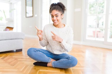Gülümseyen ve iki elleri ve parmakları ile tarafına işaret kamera bakarak yerde oturan afro saçlı güzel genç Afro-Amerikan kadın.