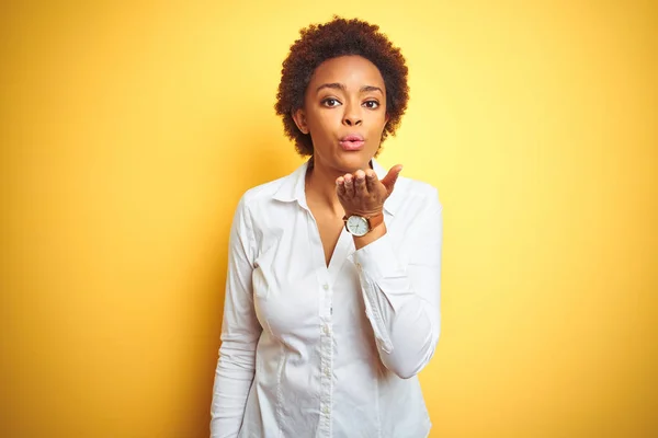 African american business woman over isolated yellow background looking at the camera blowing a kiss with hand on air being lovely and sexy. Love expression.