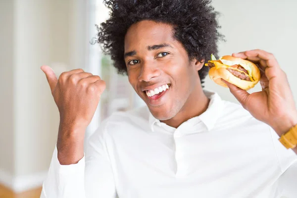 アフリカ系アメリカ人の空腹の男は 昼食のためにハンバーガーを食べて 幸せな顔を笑顔で横に親指で見せる — ストック写真