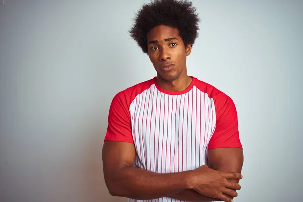 African american man with afro hair wearing red striped t-shirt over isolated white background skeptic and nervous, disapproving expression on face with crossed arms. Negative person.