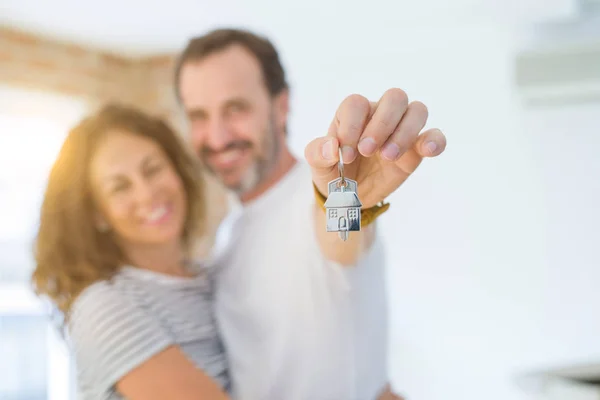 Middle age senior romantic couple holding and showing house keys, hugging and smiling happy for moving to a new home