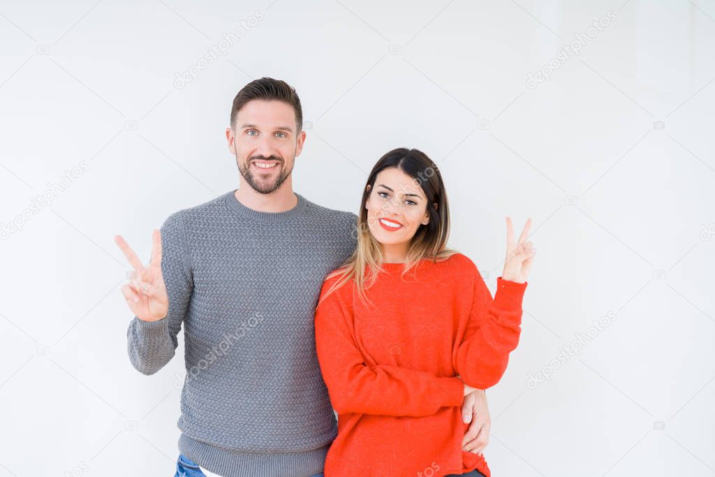 Young beautiful couple togheter over isolated background smiling with happy face winking at the camera doing victory sign. Number two.