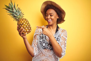 Genç African Amerikan kadın ile afro saç tutan Pineaple üzerinde sarı izole arka plan çok mutlu işaret ile el ve parmak