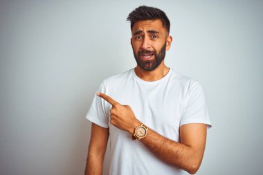 İzole beyaz arka plan üzerinde ayakta t-shirt giyen genç Hint adam bir kenara endişeli ve gergin, ilgili ve sürpriz ifade ile Işaret