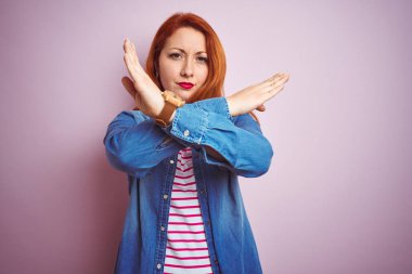 Denim gömlek ve çizgili t-shirt giyen güzel kızıl saçlı kadın izole pembe arka plan Reddi ifade geçiş kolları olumsuz işaret yapıyor, kızgın yüz