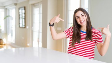 Rahat çizgili t-shirt giyen güzel genç kadın yüzünde gülümseme ile kendine güvenen görünümlü, parmaklarıyla gurur ve mutlu kendini işaret.