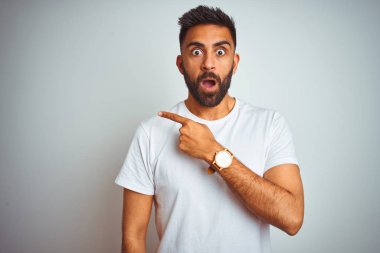 Genç Hint adam giyen t-shirt ayakta üzerinde izole beyaz arka plan sürpriz yan parmak ile işaret, açık ağız hayran ifadesi.