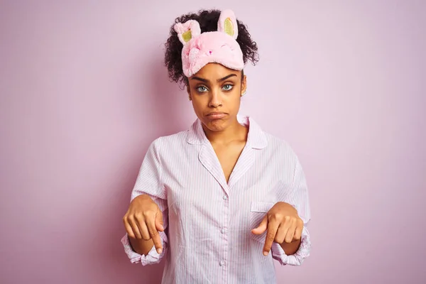 年轻的非洲裔美国妇女穿着睡衣和面具在孤立的粉红色背景指向向下看悲伤和沮丧 指示方向用手指 不快乐和沮丧 — 图库照片