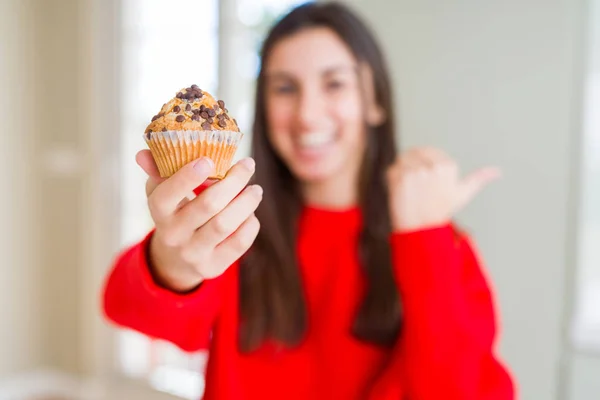 チョコレートチップマフィンを食べる美しい若い女性は 幸せそうな顔で横に親指で見せて — ストック写真