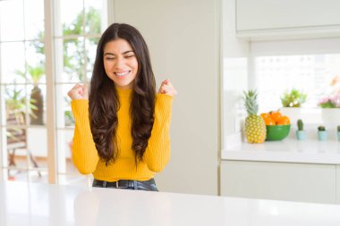 Beyaz masada evde genç güzel kadın zafer gülümseyen kutlamak kaldırdı silah ile başarı için heyecanlı. Kazanan kavramı.