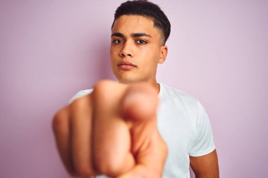 İzole pembe arka plan üzerinde duran t-shirt giyen genç Brezilyalı adam kameraya parmak la işaret ve size, el işareti, önden olumlu ve kendinden emin jest