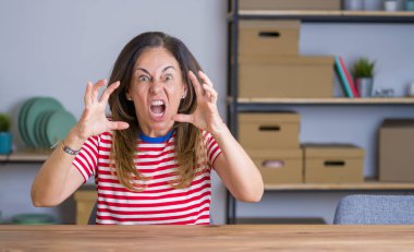 Orta yaş üst düzey kadın evde masada oturan öfke ile sinirli, elleri boğmaya çalışıyor, deli bağırarak bağırıyor