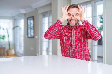 Renkli gömlek giyen yakışıklı adam dürbün yapışması gibi ok jest yapıyor, gözleri parmaklarla bakıyor. Çılgın ifade.