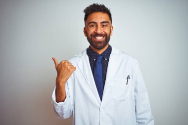 Genç Hint Doktor adam ayakta üzerinde izole beyaz arka plan gülümseyen ile mutlu yüz seyir ve işaret yanında ile Thumb yukarı.