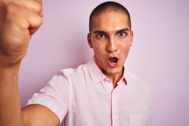 Pembe izole arka plan üzerinde zarif gömlek giyen genç yakışıklı adam rahatsız ve öfke, deli ve yükseltilmiş el, öfke kavramı ile bağırarak bağırıyor sinirli