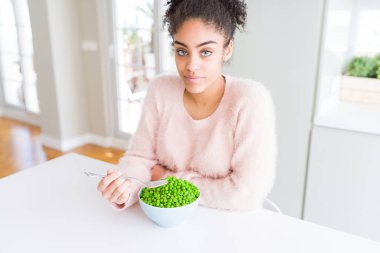 Genç Afrikalı Amerikalı kız ciddi düşünme akıllı yüz üzerinde güvenli bir ifade ile sağlıklı yeşil bezelye yeme