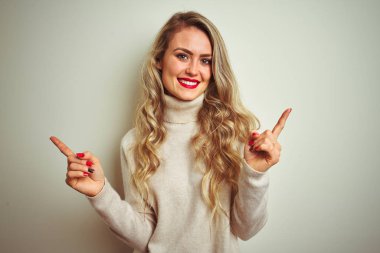 Güzel kadın izole beyaz arka plan üzerinde kış balıkçı yaka kazak giyiyor farklı yönlere parmaklar ile işaret emin gülümseyen. Reklam için alanı Kopyala