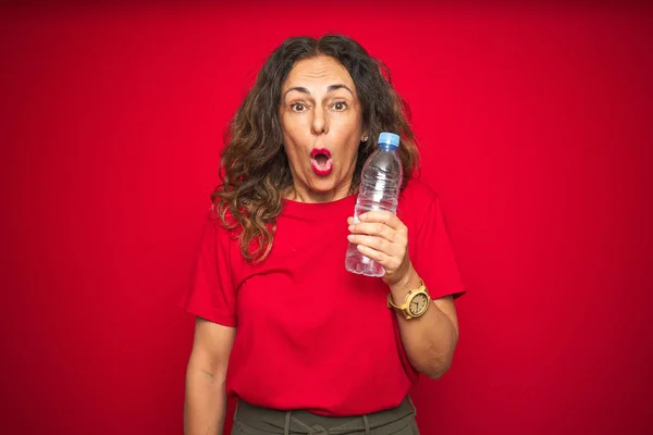 Seniorin Mittleren Alters Mit Plastikwasserflasche Über Rotem Isoliertem Hintergrund Erschrocken — Stockfoto