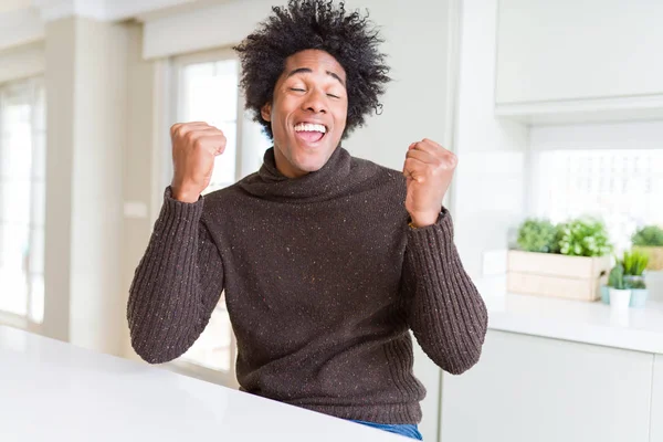 冬のセーターを着たアフリカ系アメリカ人男性は 腕を上げ 笑顔を浮かべて 成功のために叫んで勝者のジェスチャーをして非常に幸せで興奮しています お祝いのコンセプト — ストック写真