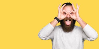 Rahat kazak giyen genç sarışın adam dürbün yapışması gibi ok jest yapıyor, gözleri parmaklarla bakıyor. Çılgın ifade.