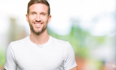 Yakışıklı adam yüzünde mutlu ve güzel bir gülümseme ile rahat beyaz t-shirt giyiyor. Şanslı kişi.