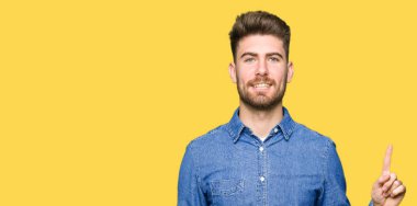 Genç yakışıklı sarışın adam giyiyor rahat kot gömlek gösterme ve kendinden emin ve mutlu gülümseyen bir parmak ile işaret eden oktan yukarı.