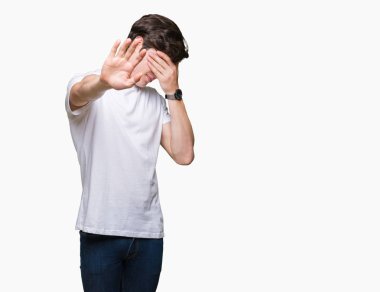 Yakışıklı delikanlı üzerinde rahat beyaz t-shirt giyen izole elleriyle gözlerini kapsayan arka plan ve stop jest ile acı ve korku ifadesi. Utandım ve negatif kavramı.