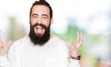 Uzun saç ve sakal deli ve çığlık kaldırdı ve açık gözleri heyecanlı silah ile başarı için hayran sportif kazak kutluyor giyen genç adam. Kazanan kavramı