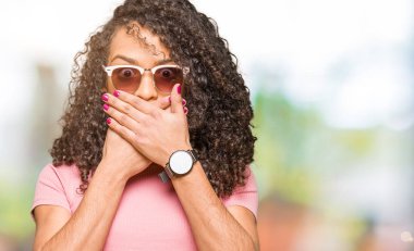 Genç güzel kadın kıvırcık saçlı ağız hata için elleriyle kapsayan şok pembe güneş gözlüğü takıyor. Gizli kavramı.