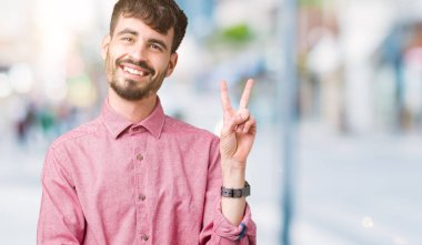 Genç yakışıklı adam izole arka plan üzerinde pembe gömlek giyen mutlu yüz zafer işareti yapıyor kamera göz kırpıyor ile gülümsüyor. İki numara.