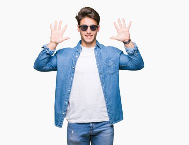 Yakışıklı delikanlı üzerinde güneş gözlüğü takıyor gösterilen arka plan izole ve parmakları ile işaret kendinden emin ve mutlu gülümseyerek süre on numara.