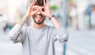 Dilini, parmaklarının arasından baktığını yapışmasını dürbün gibi ok jest yapıyor izole arka plan üzerinde sweatshirt giyen genç yakışıklı adam. Deli ifade.