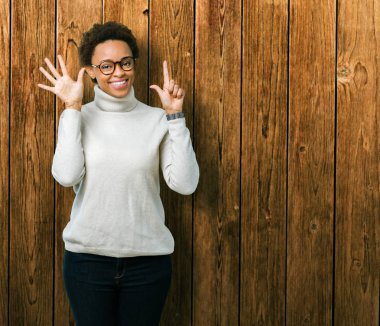 Genç güzel Afrikalı-Amerikalı kadın gözlük gösterilen ve parmakları ile işaret izole arka plan üzerinde kendinden emin ve mutlu gülümseyerek süre yedi numara.