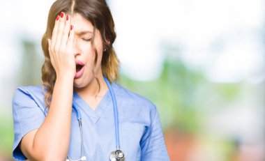 Tıbbi üniforma Yawning giyen genç yetişkin doktor kadın yarım yüz, göz ve ağız el ile kapsayan yorgun. Acı yüzü acıyor.
