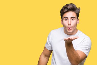 Bir öpücük el ile güzel ve seksi olmak hava üfleme kamera bakarak izole arka plan üzerinde beyaz t-shirt giyen genç yakışıklı adam. Aşk ifade.