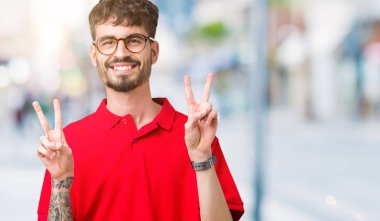 Zafer işareti yapıyor parmak gösterilen kamera seyir gülümseyen izole arka plan üzerinde gözlük takan yakışıklı delikanlı. İki numaralı.