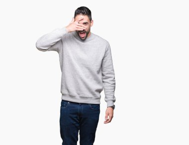 Mahcup ifadeyle parmaklarımın arasından seyir yüz ve gözler el ile kapsayan şok bakmak izole arka plan üzerinde sweatshirt giyen genç yakışıklı adam.