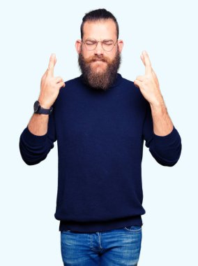 Gözlük ve balıkçı yaka kazak giyen genç sarışın adam umut ve gözler kapalı parmakları geçiş gülümseyen. Şans ve batıl fikir.