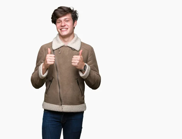 年轻的帅哥穿着冬衣在孤立的背景成功标志做积极的手势 竖起大拇指微笑和快乐 带着欢快的表情 获胜者的手势看着镜头 — 图库照片