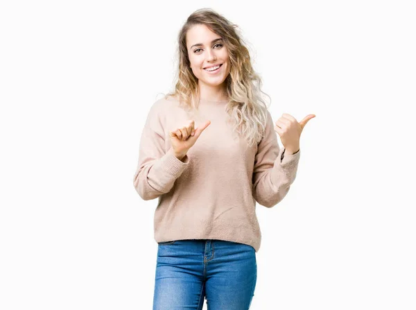 孤立した背景の上にセーターシャツを着た美しい若いブロンドの女性は 手と親指で後ろを指し 自信を持って微笑む — ストック写真