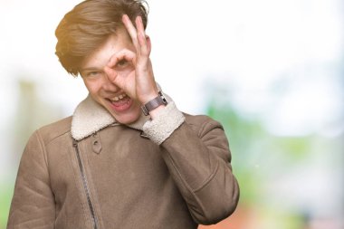 Gülümseyen, parmakları ile mutlu yüz üzerinden seyir göz el ile ok jest yapıyor izole arka plan üzerinde kış ceket giyen genç yakışıklı adam.