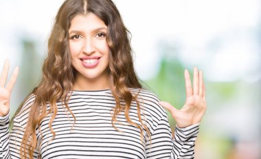 Gösterilen ve parmakları ile işaret genç güzel kadın giyiyor çizgili süveter numara 9 kendinden emin ve mutlu gülümseyerek süre.