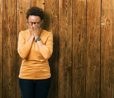 Üzgün ifade yüz eller ile ağlayarak süre kapsayan ile izole arka plan üzerinde gözlük takan genç güzel Afrikalı-Amerikalı kadın. Depresyon kavramı.
