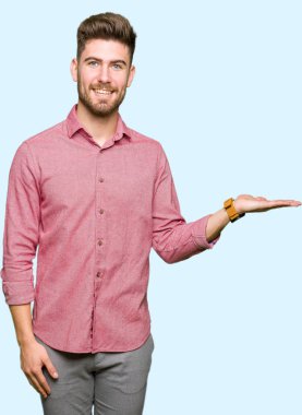 Genç yakışıklı iş casual adam gülümseyen neşeli sunulması ve kameraya bakarak avucunun ile işaret.