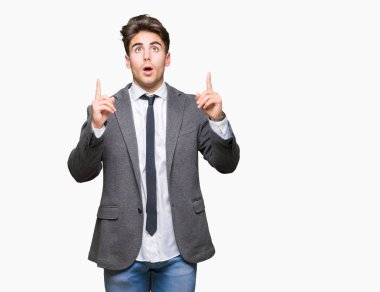 Giyen genç iş adamı takım elbise ve kravat hayrete ve yukarıya bakıyor ve parmakları ile işaret ve silah kaldırdı sürpriz izole arka plan üzerinde.